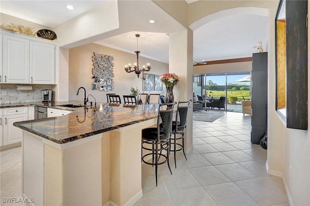 kitchen with sink, a breakfast bar area, dark stone countertops, white cabinetry, and kitchen peninsula