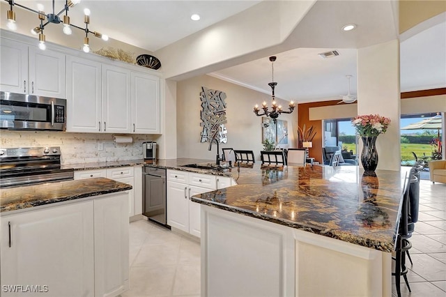 kitchen featuring a breakfast bar, dark stone countertops, white cabinets, hanging light fixtures, and stainless steel appliances