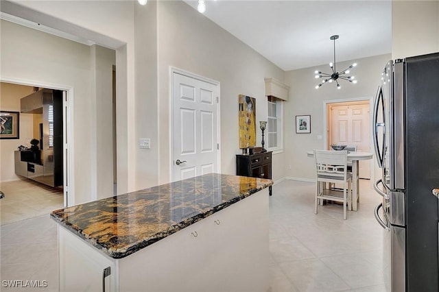 kitchen featuring a center island, a chandelier, light tile patterned floors, stainless steel refrigerator, and dark stone countertops