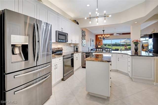 kitchen with stainless steel appliances, kitchen peninsula, hanging light fixtures, and dark stone countertops