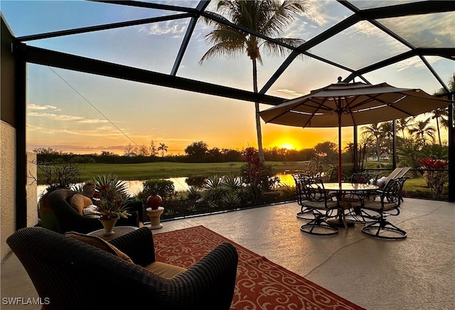 patio terrace at dusk featuring a water view and glass enclosure