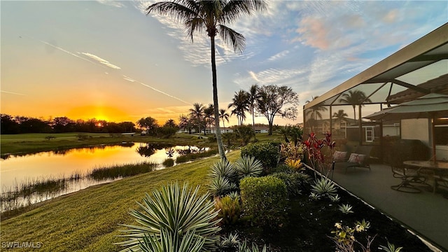 yard at dusk featuring a water view and glass enclosure