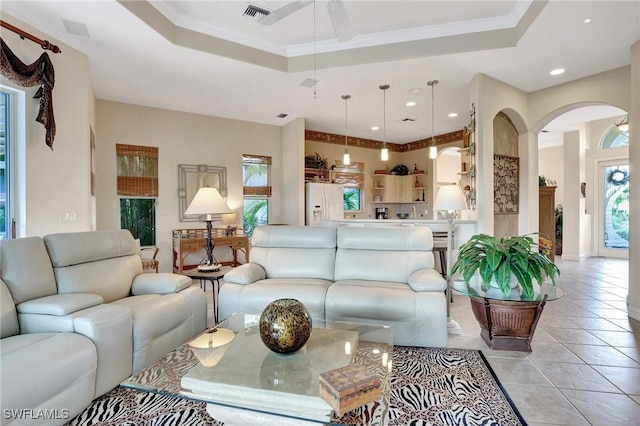 living room featuring light tile patterned flooring, ceiling fan, ornamental molding, and a raised ceiling