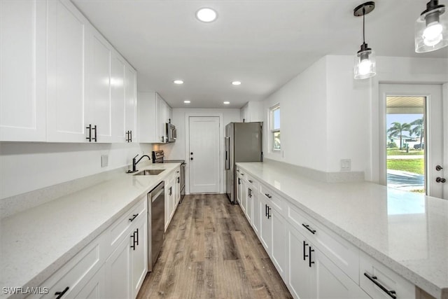 kitchen with light wood finished floors, white cabinets, appliances with stainless steel finishes, a sink, and recessed lighting