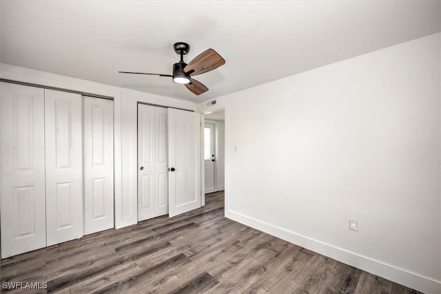 unfurnished bedroom with visible vents, baseboards, ceiling fan, wood finished floors, and two closets