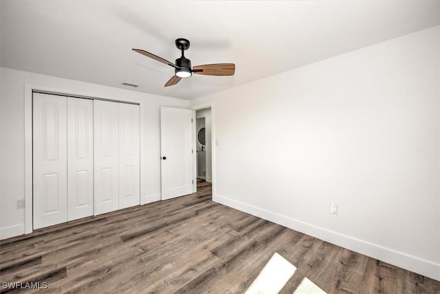 unfurnished bedroom featuring a closet, baseboards, stacked washer / drying machine, and wood finished floors