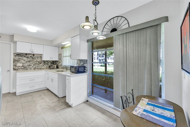 kitchen with light tile patterned flooring, sink, hanging light fixtures, white cabinets, and backsplash