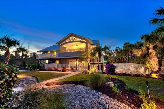 back house at dusk with a yard, ceiling fan, and a balcony