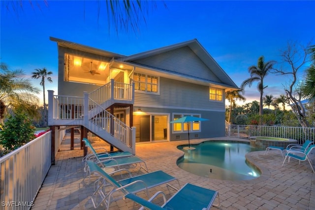 back house at dusk with ceiling fan, a patio, and a pool with hot tub