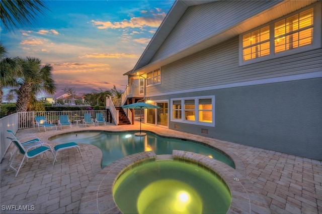 pool at dusk featuring an in ground hot tub and a patio area