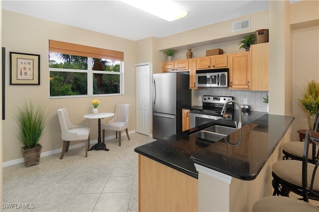 kitchen with sink, appliances with stainless steel finishes, kitchen peninsula, dark stone counters, and backsplash