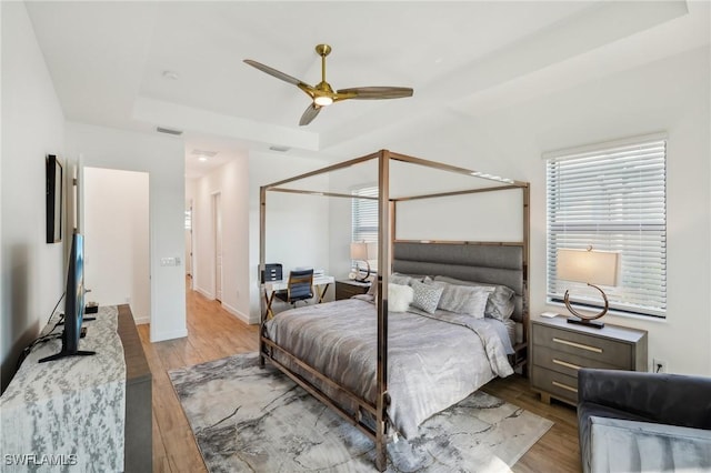 bedroom with ceiling fan, a tray ceiling, light hardwood / wood-style floors, and a closet