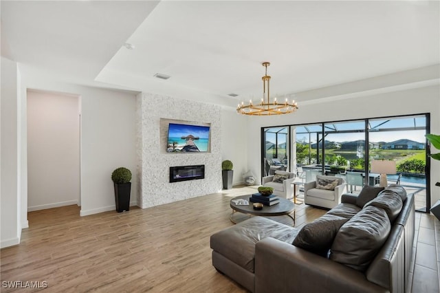 living room featuring a raised ceiling, light wood-type flooring, a notable chandelier, and a fireplace