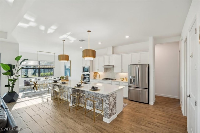 kitchen featuring pendant lighting, white cabinetry, an island with sink, a kitchen bar, and stainless steel appliances