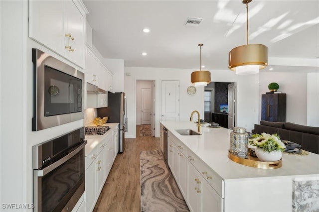 kitchen with white cabinetry, appliances with stainless steel finishes, an island with sink, and hanging light fixtures