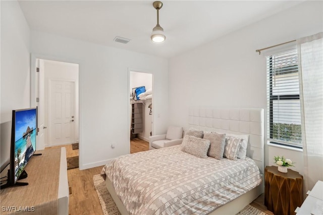 bedroom with a walk in closet, light wood-type flooring, and a closet