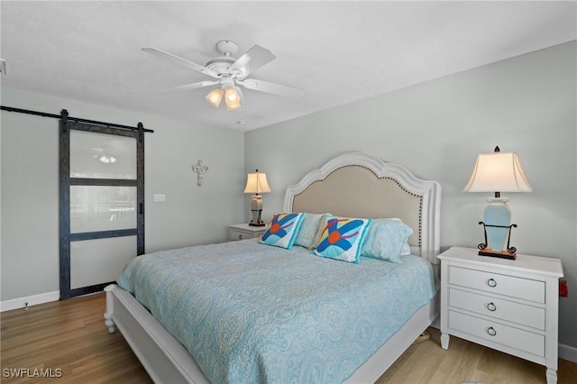 bedroom with ceiling fan, a barn door, and light hardwood / wood-style floors