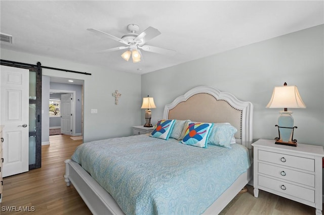 bedroom featuring hardwood / wood-style flooring, a barn door, and ceiling fan