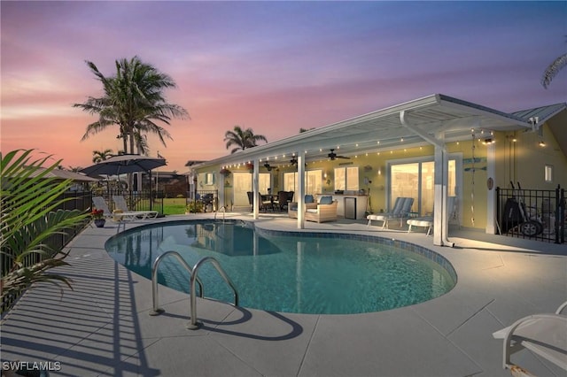 pool at dusk with ceiling fan and a patio area