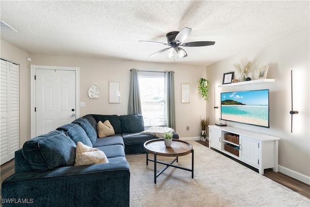 living room with a ceiling fan, baseboards, wood finished floors, visible vents, and a textured ceiling