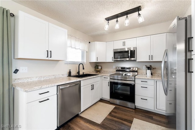 kitchen with sink, appliances with stainless steel finishes, white cabinetry, a textured ceiling, and dark hardwood / wood-style flooring