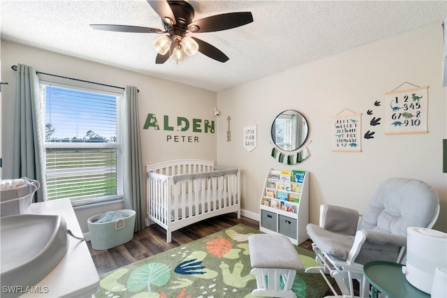 bedroom featuring ceiling fan, a nursery area, dark hardwood / wood-style floors, and a textured ceiling