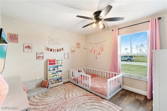 bedroom featuring ceiling fan, hardwood / wood-style floors, a textured ceiling, and a crib