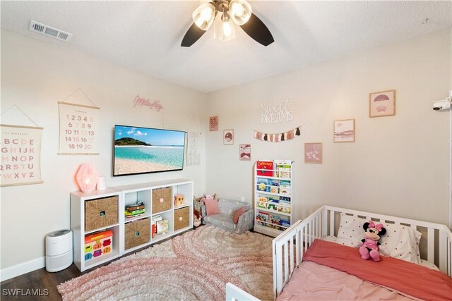 bedroom featuring ceiling fan, wood-type flooring, a textured ceiling, and a crib