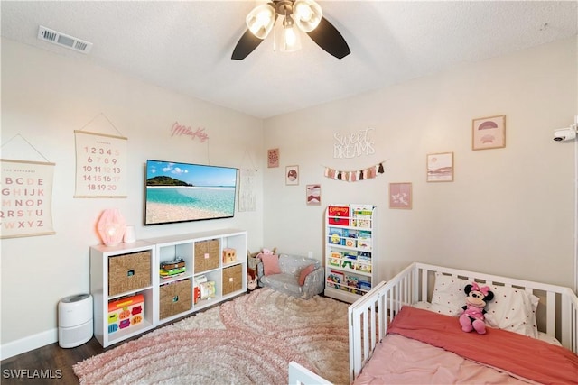 bedroom featuring visible vents, a crib, baseboards, ceiling fan, and wood finished floors