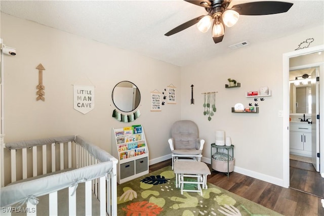 bedroom with ceiling fan, dark hardwood / wood-style floors, sink, and a crib