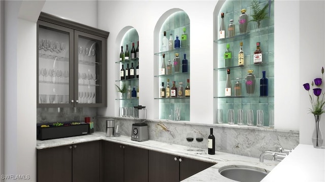 bar featuring tasteful backsplash, dark brown cabinets, sink, and light stone counters