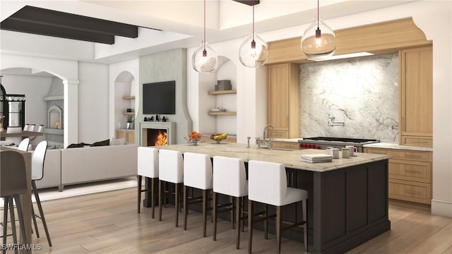 kitchen featuring decorative light fixtures, wood-type flooring, an island with sink, and a kitchen bar