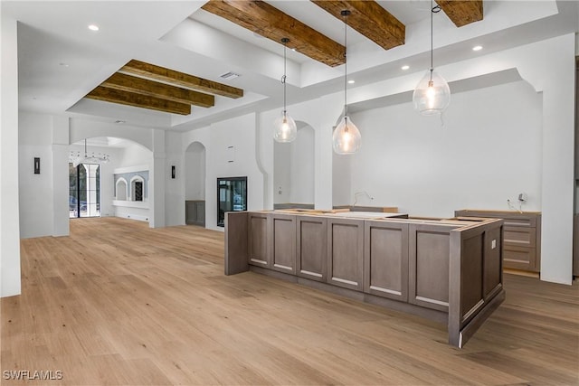 kitchen with pendant lighting, a kitchen island with sink, light hardwood / wood-style flooring, and beamed ceiling