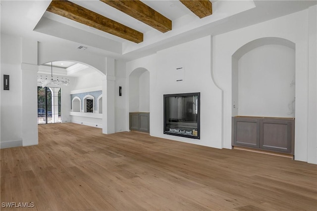 unfurnished living room featuring a raised ceiling, beamed ceiling, and light wood-type flooring