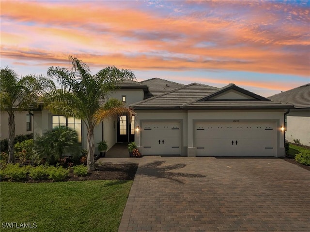 view of front of property with decorative driveway, a tile roof, an attached garage, and stucco siding