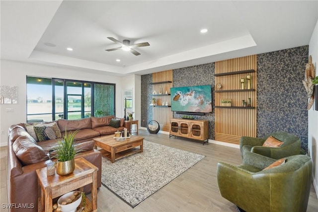 living room with a tray ceiling, light wood-type flooring, and recessed lighting