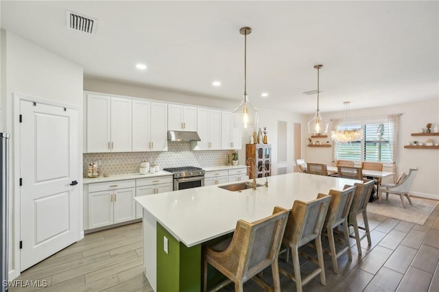 kitchen featuring visible vents, a sink, under cabinet range hood, backsplash, and gas stove