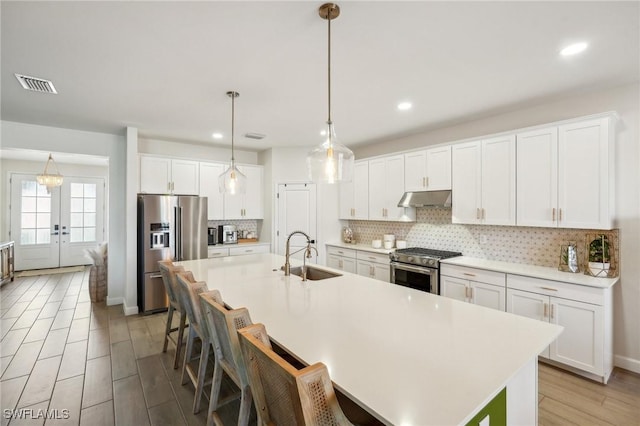 kitchen with under cabinet range hood, stainless steel appliances, a sink, visible vents, and tasteful backsplash