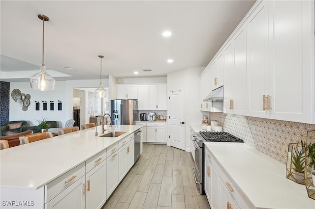 kitchen featuring decorative backsplash, appliances with stainless steel finishes, a sink, light wood-type flooring, and under cabinet range hood