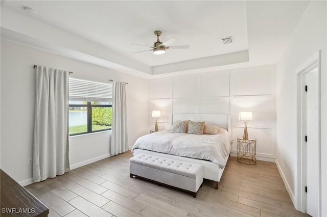 bedroom featuring a raised ceiling, visible vents, a decorative wall, light wood-style flooring, and baseboards