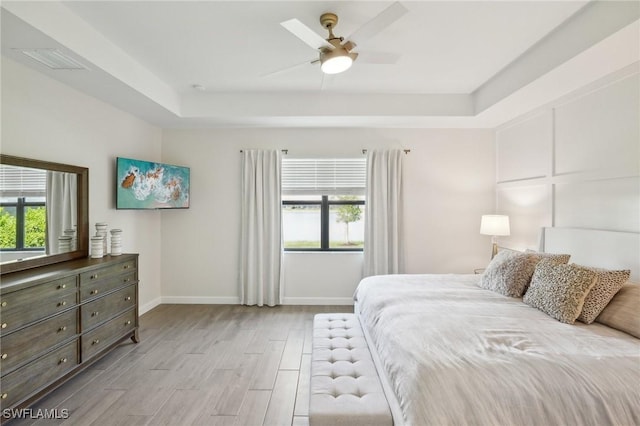 bedroom with a ceiling fan, visible vents, baseboards, light wood finished floors, and a raised ceiling