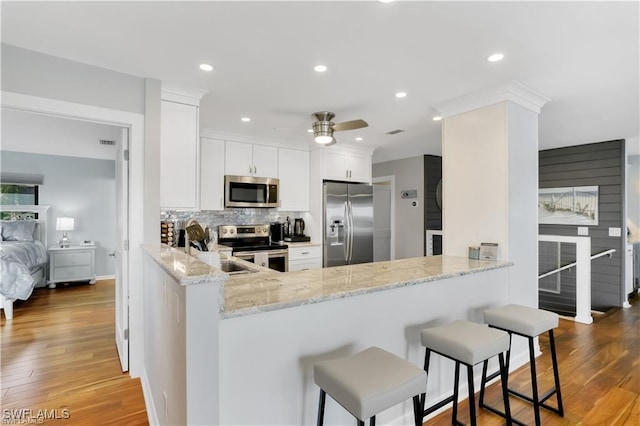 kitchen featuring light stone countertops, appliances with stainless steel finishes, white cabinets, and kitchen peninsula