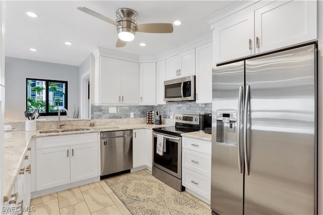 kitchen with light stone counters, stainless steel appliances, a sink, white cabinetry, and a ceiling fan