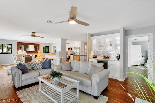 living room with ceiling fan, indoor bar, beverage cooler, and dark hardwood / wood-style flooring