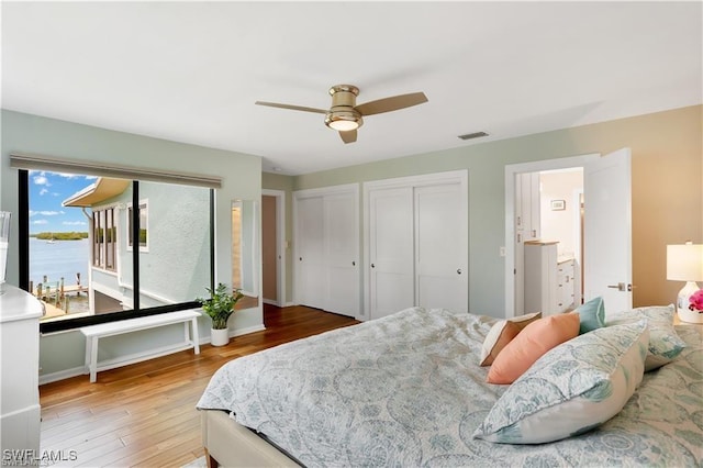 bedroom with multiple closets, wood-type flooring, a water view, and ceiling fan