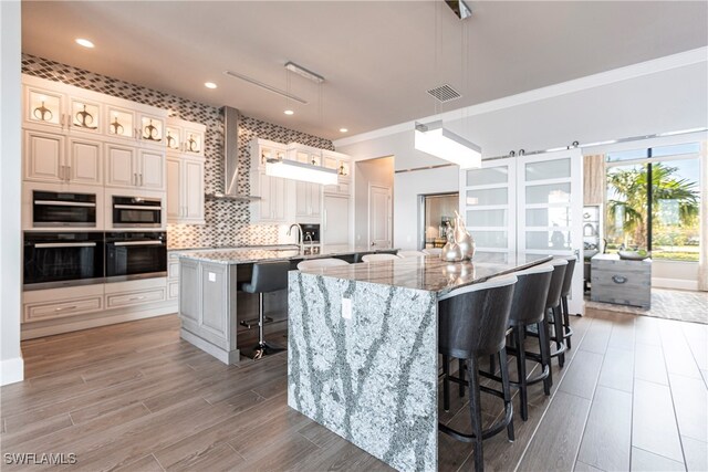 kitchen featuring hanging light fixtures, light stone countertops, wall chimney range hood, a breakfast bar, and a spacious island