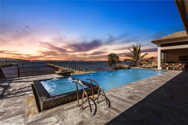 pool at dusk featuring pool water feature, a water view, and a patio area