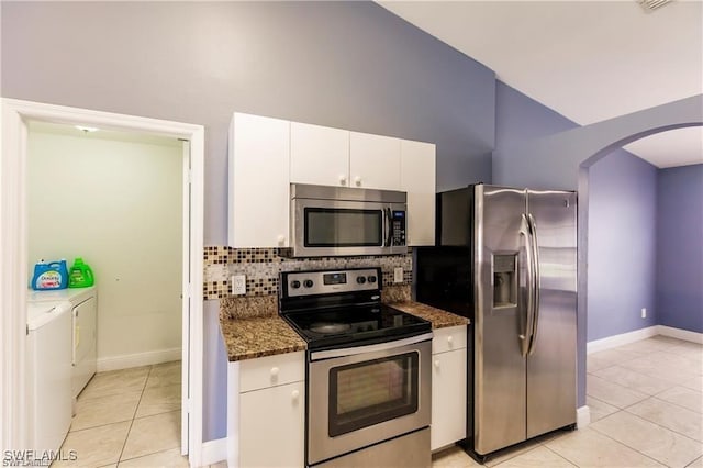 kitchen with appliances with stainless steel finishes, washer and dryer, dark stone countertops, white cabinets, and backsplash