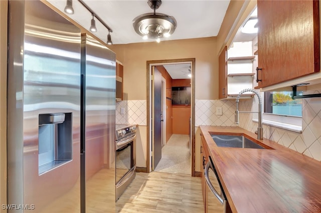 kitchen with appliances with stainless steel finishes, butcher block counters, sink, decorative backsplash, and light hardwood / wood-style flooring