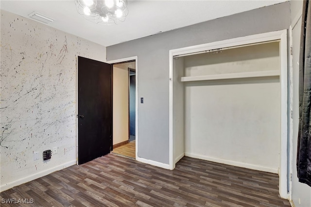 unfurnished bedroom featuring dark hardwood / wood-style floors, a notable chandelier, and a closet